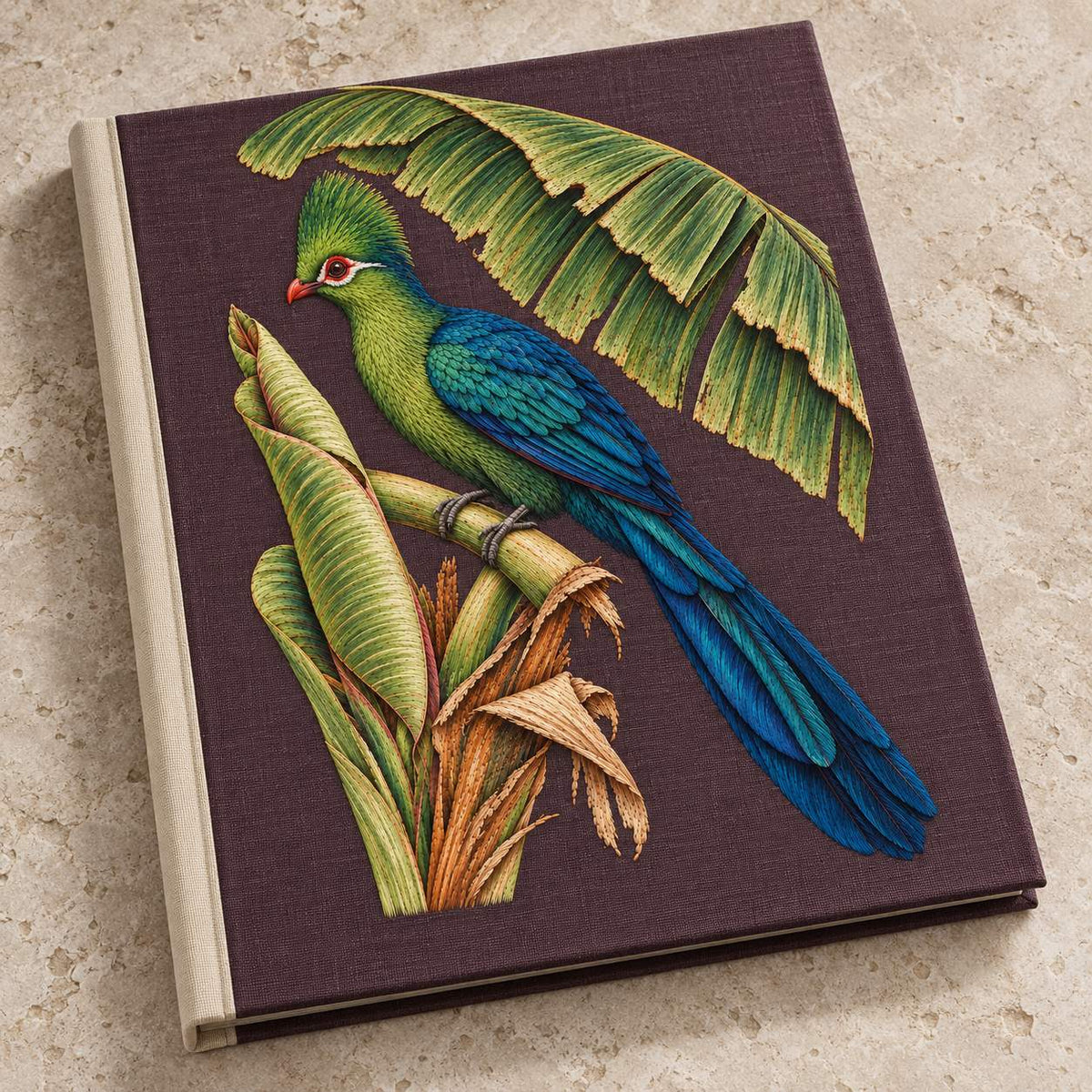 Turaco Beneath the Banana Rib Fan visual mockup shown on a cloth portfolio cover, with the design on deep plum linen.