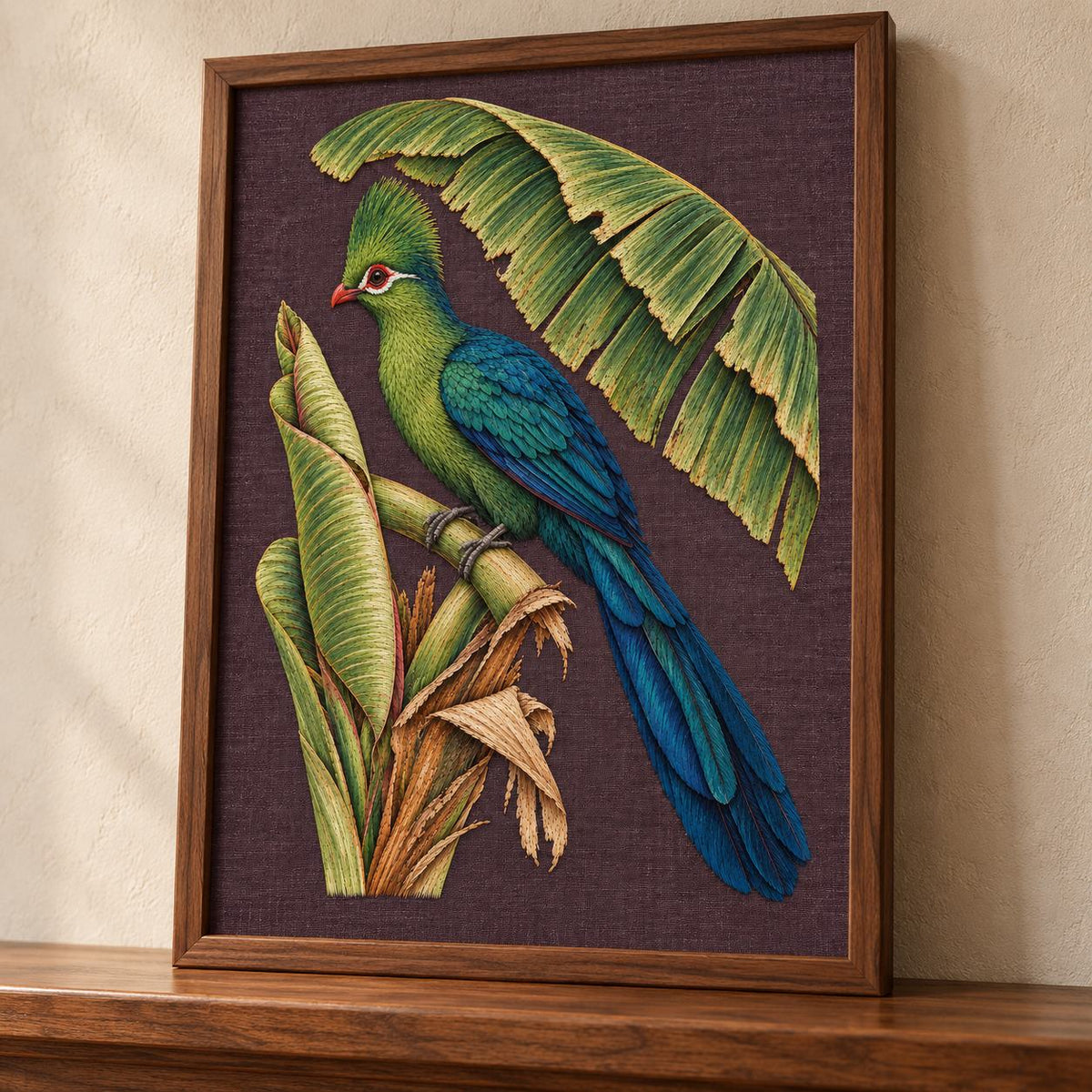 Turaco Beneath the Banana Rib Fan visual mockup shown in a frame leaning on a mantel, with the design on deep plum linen.