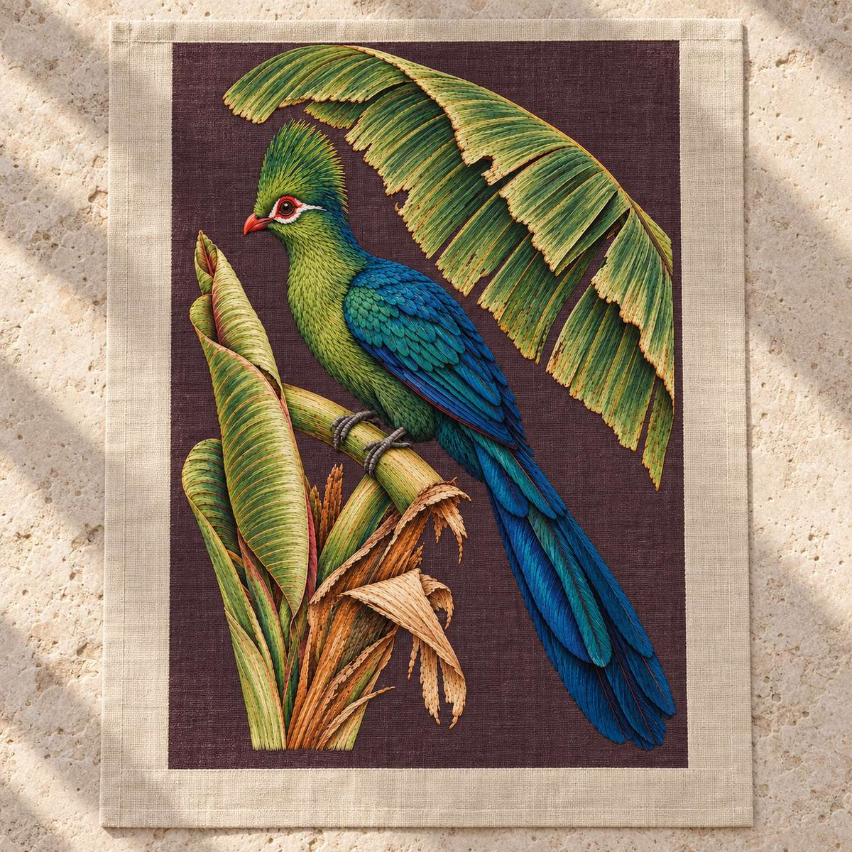 Turaco Beneath the Banana Rib Fan visual mockup shown as a textile panel on a stone platform, with the design on deep plum linen.