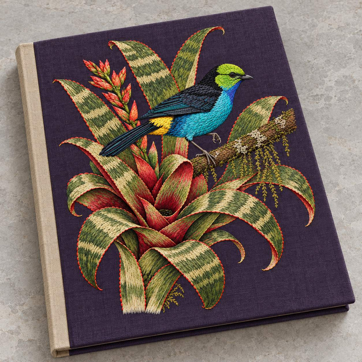 Paradise Tanager in the Bromeliad Wheel visual mockup shown on a cloth portfolio cover, with the design on deep violet-slate linen.