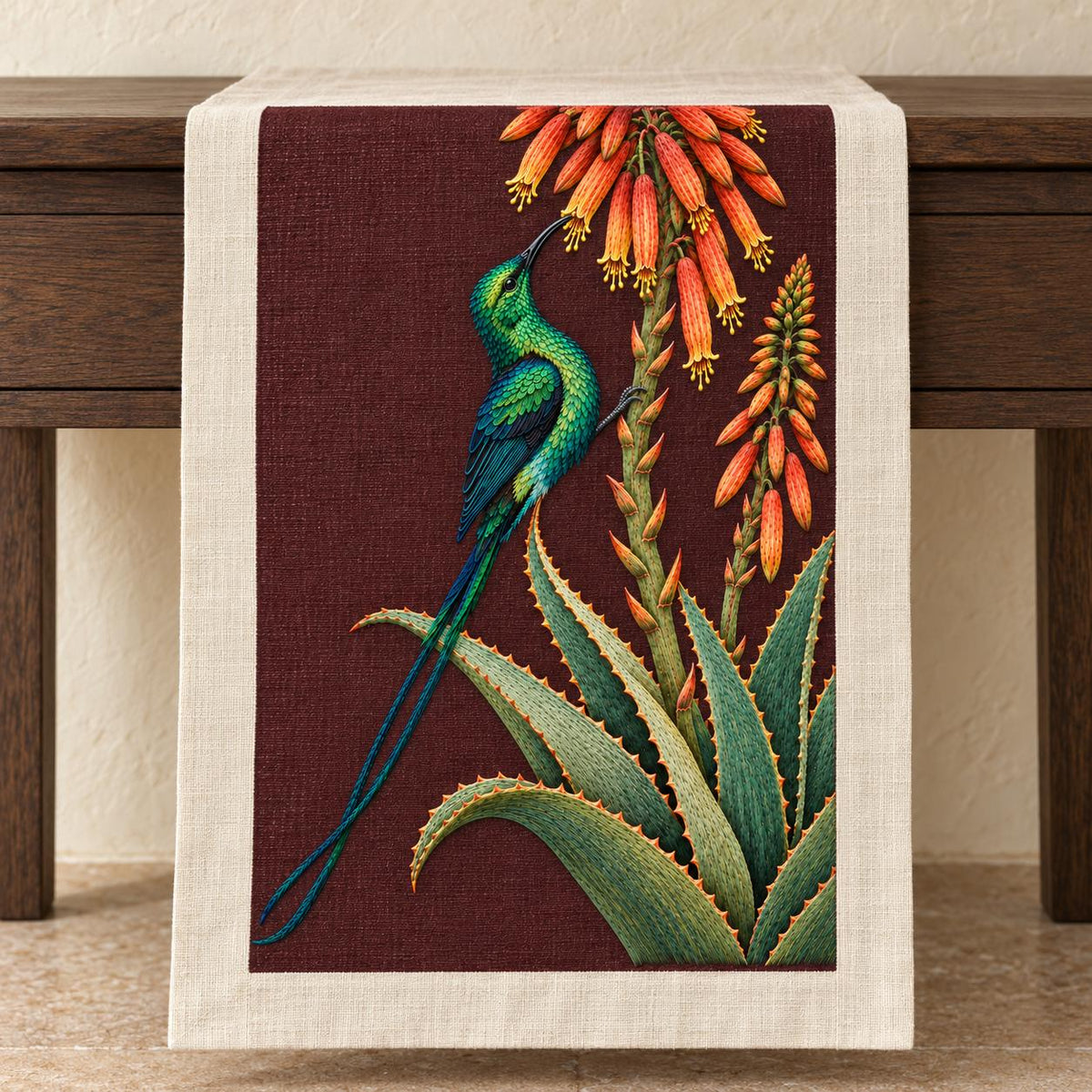 Sunbird at the Copper Aloe visual mockup shown on a textile runner over a console, with the design on dark burgundy linen.