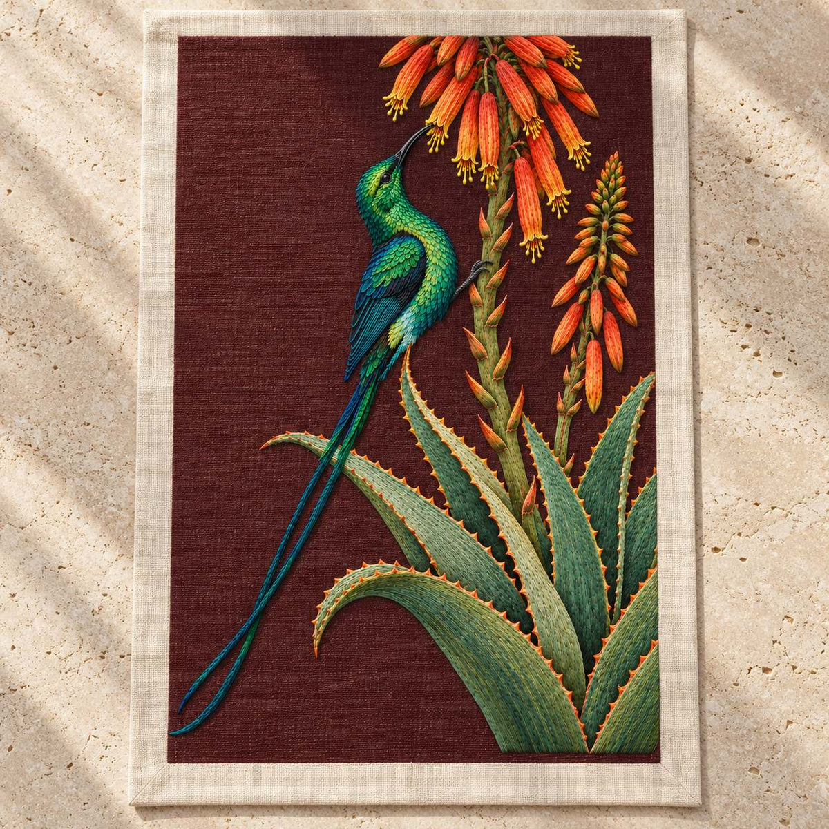 Sunbird at the Copper Aloe visual mockup shown as a textile panel on a stone platform, with the design on dark burgundy linen.