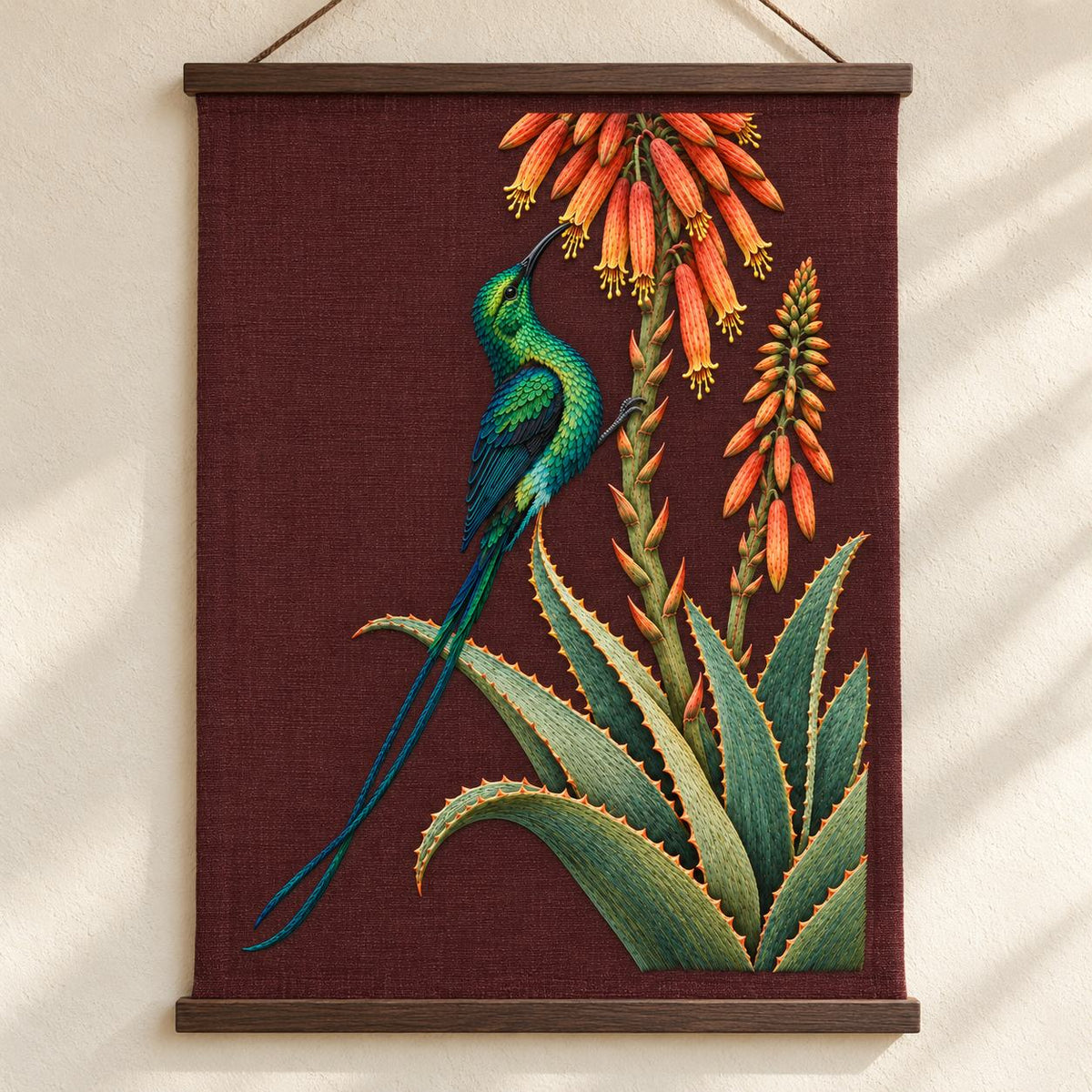 Sunbird at the Copper Aloe visual mockup shown as a hanging textile held by wooden rails, with the design on dark burgundy linen.