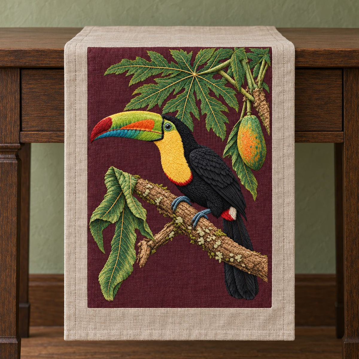 Toucan Under the Papaya Canopy visual mockup shown on a textile runner over a console, with the design on deep burgundy linen.