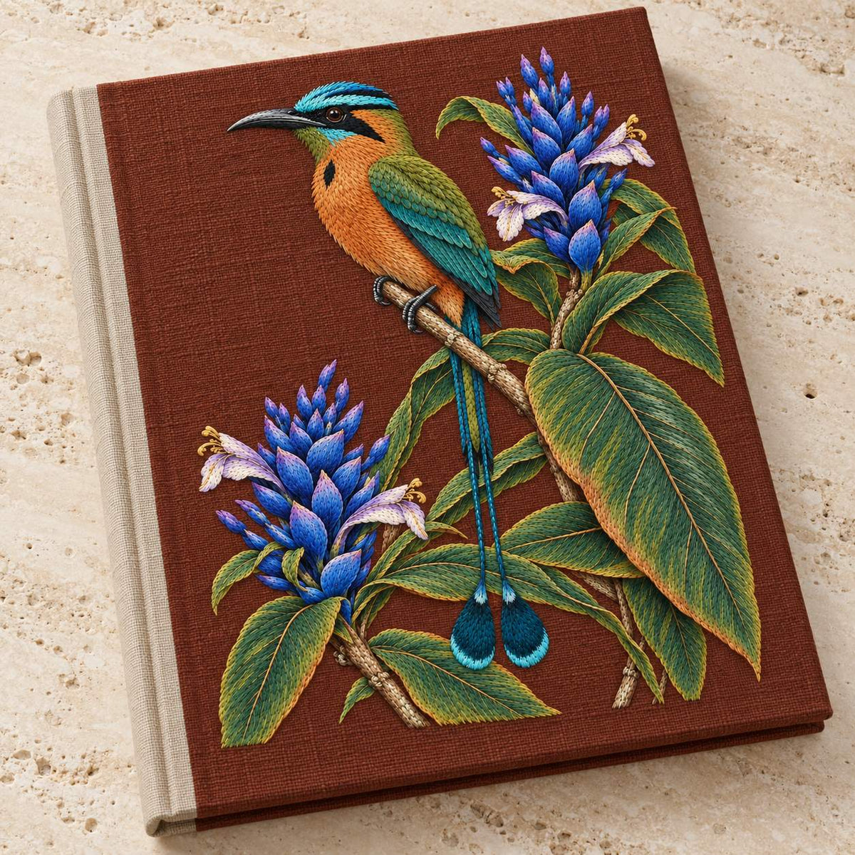 Motmot at the Blue Ginger Stair visual mockup shown on a cloth portfolio cover, with the design on muted rust linen.