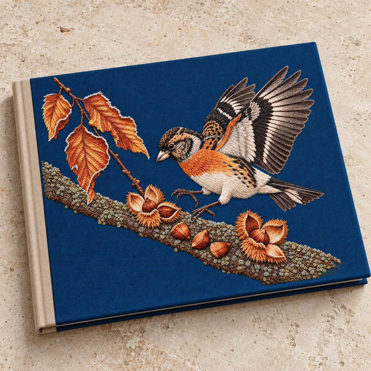 Brambling Above the Frosted Beech Mast visual mockup shown on a cloth portfolio cover, with the design on deep-blue linen.
