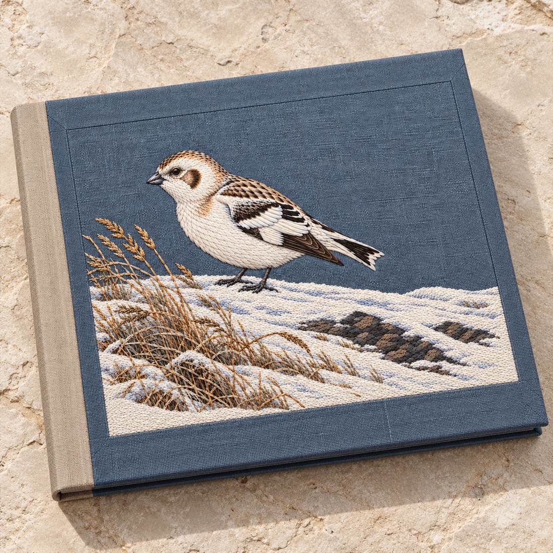Snow Bunting at the Wind Scoured Drift visual mockup shown on a cloth portfolio cover, with the design on blue-grey linen.