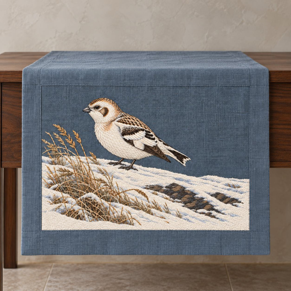 Snow Bunting at the Wind Scoured Drift visual mockup shown on a textile runner over a console, with the design on blue-grey linen.