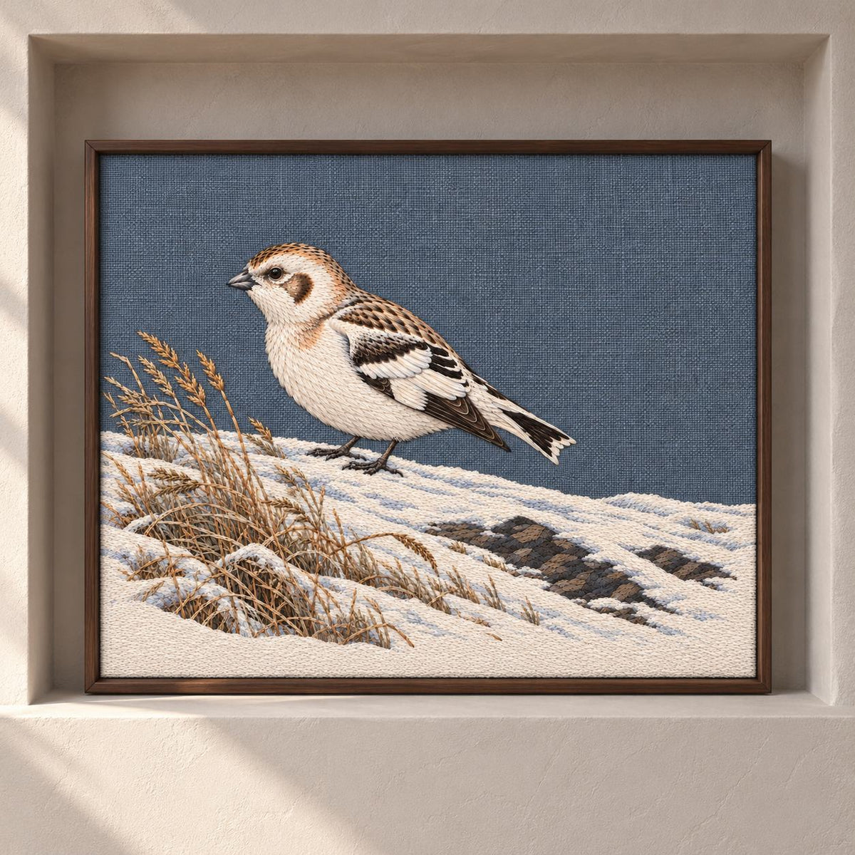 Snow Bunting at the Wind Scoured Drift visual mockup shown as a framed textile in a gallery niche, with the design on blue-grey linen.