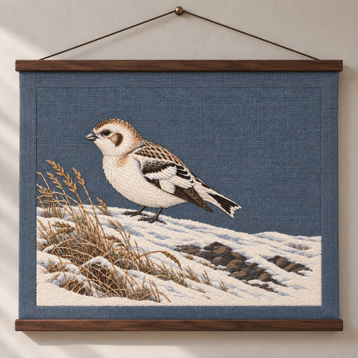 Snow Bunting at the Wind Scoured Drift visual mockup shown as a hanging textile held by wooden rails, with the design on blue-grey linen.
