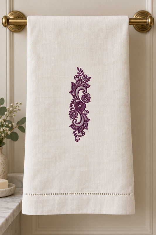 Styled linen guest towel mockup with a single deep muted aubergine purple lace scroll floral ornament embroidered on pale linen; the complete motif has clear fabric around it.