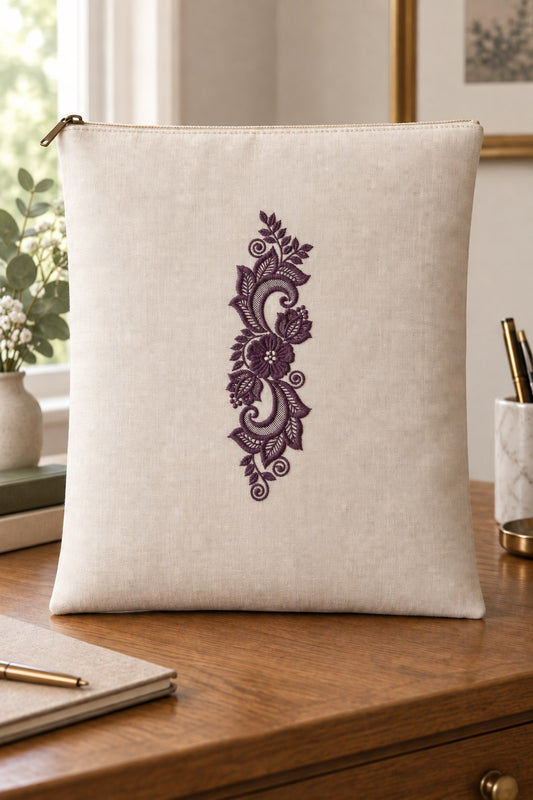 Styled linen zip folio mockup with a single deep muted aubergine purple lace scroll floral ornament embroidered on pale linen; the complete motif has clear fabric around it.