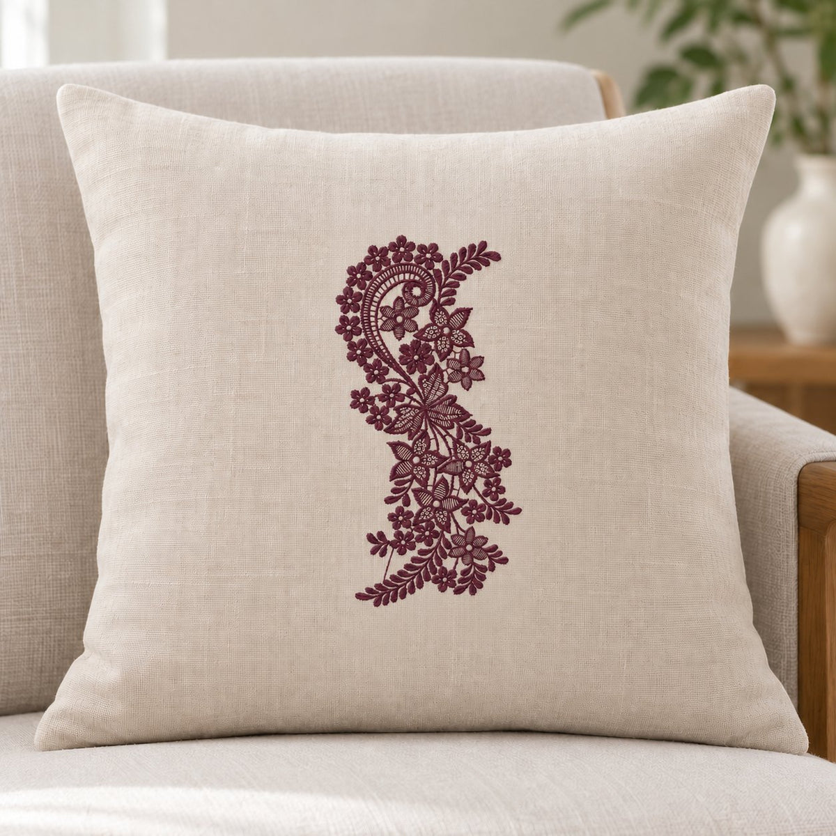 Ivory square cushion with a centered upright aubergine paisley vine and delicate floral mesh embroidery.