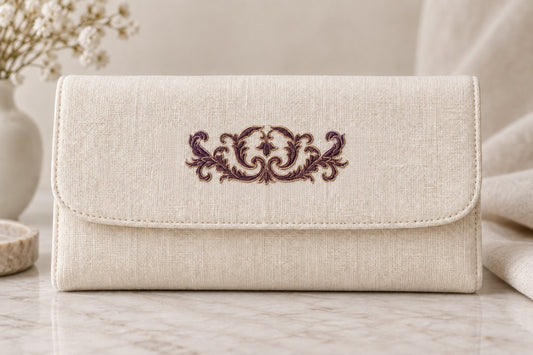 Ivory linen clutch with a small symmetrical aubergine acanthus crest and pale edging on the flap.
