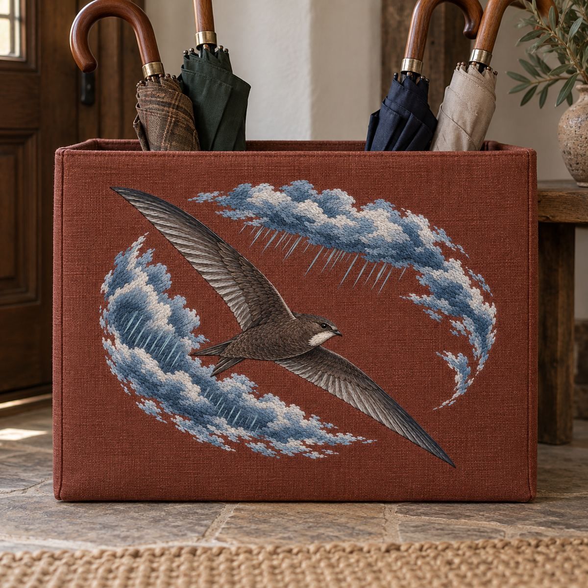 Swift embroidery design in a digital mockup of large flat landscape rust linen umbrella-storage box front with umbrellas behind and above. Placement inspiration for Study 02.