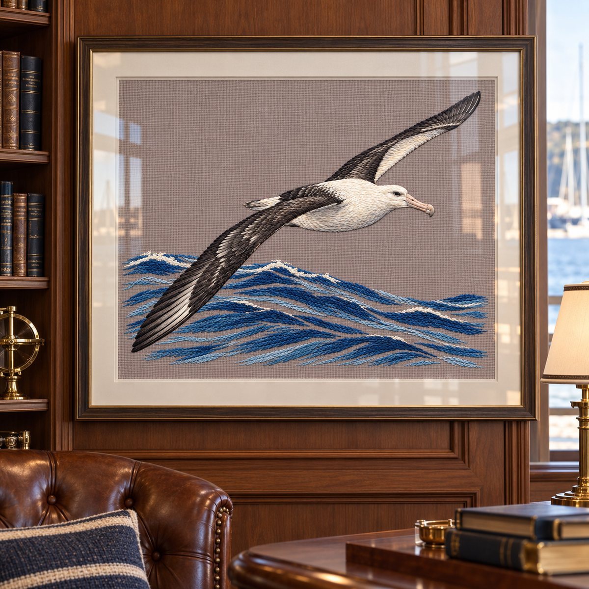 Albatross embroidery design shown in a digital mockup of wide framed textile under glass in a yacht-club reading room, subtle reflections. Study 03.