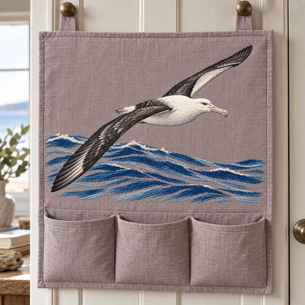 Albatross embroidery design in a digital mockup of broad taupe linen cabin door organizer with pockets below full embroidered field. Placement inspiration for Study 03.