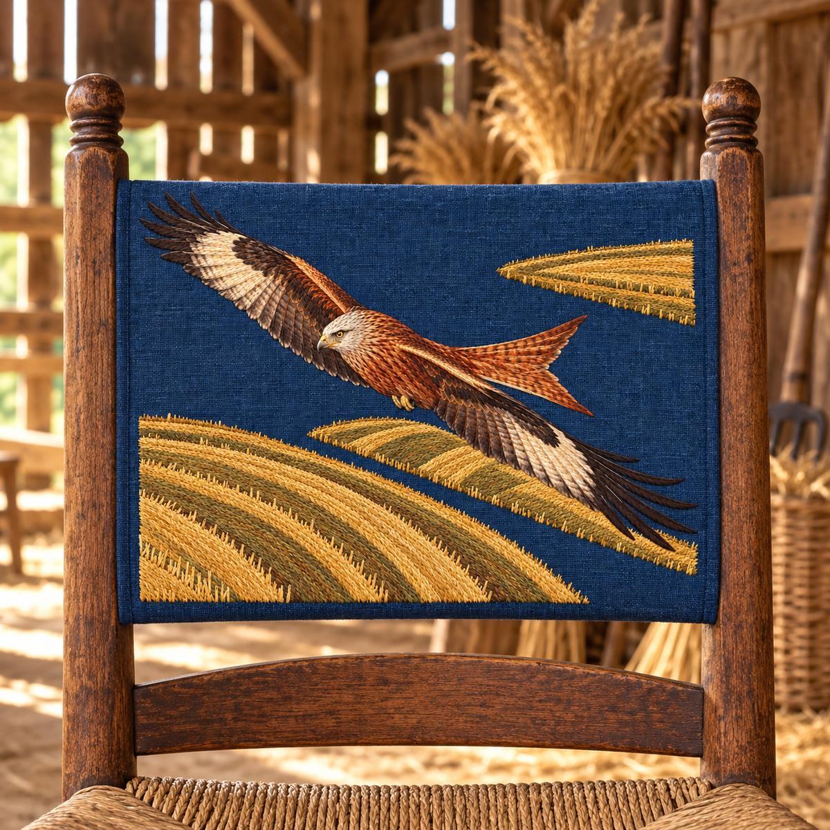 Kite embroidery design in a digital mockup of An indigo rectangular chair-back slip panel on a rustic ladderback chair in a wheat-drying barn. Placement inspiration for Study 05.
