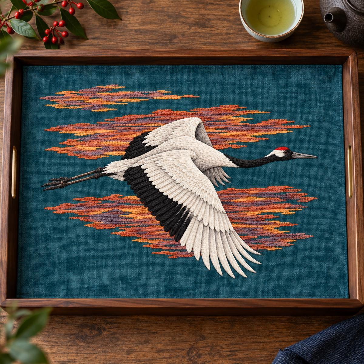 Crane embroidery design in a digital mockup of A blue-green linen rectangular tea tray cloth displayed flat in a large open wooden tray, shot overhead, cups outside the embroidered field. Placement inspiration for Study 07.