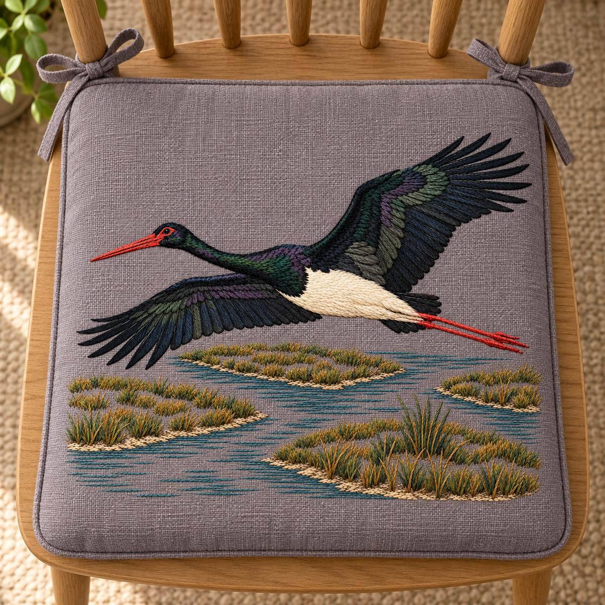 Black Stork embroidery design in a digital mockup of A plum-grey linen chair-seat pad viewed directly overhead on a plain oak chair; head left, marsh bottom of photo, no sideways rotation. Placement inspiration for Study 08.