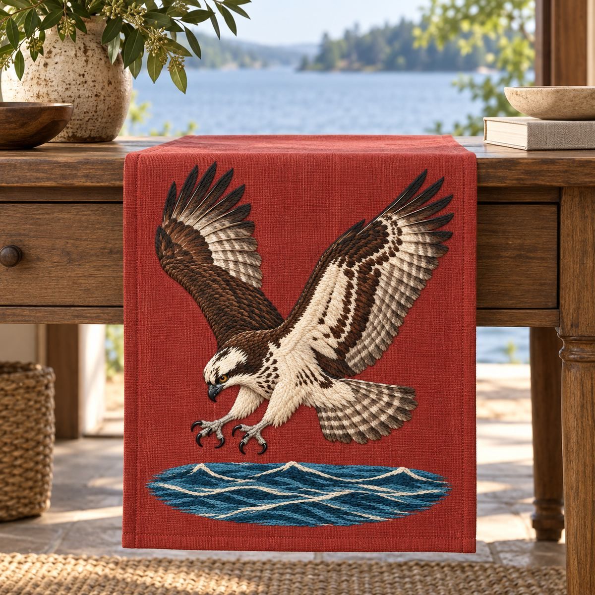 Osprey embroidery design in a digital mockup of A terracotta linen vertical runner end hanging straight from a lakeside console, entire portrait design on the hanging end with water below feet. Placement inspiration for Study 09.