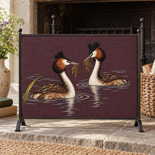 Grebe Pair embroidery design shown in a digital mockup of A single horizontal linen fire-screen panel in a slim dark iron freestanding frame in a summer cottage, unlit fireplace, diffuse morning light, full design unobstructed. Study 15.
