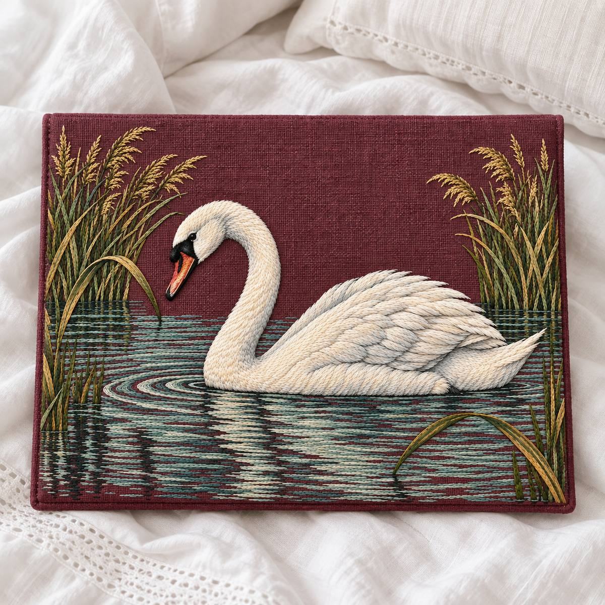 Mute Swan embroidery design in a digital mockup of A landscape embroidered lingerie storage envelope, flat front and closure on reverse, lying on a white linen bed with the complete swan visible, elegant restrained styling. Placement inspiration for Study 31.