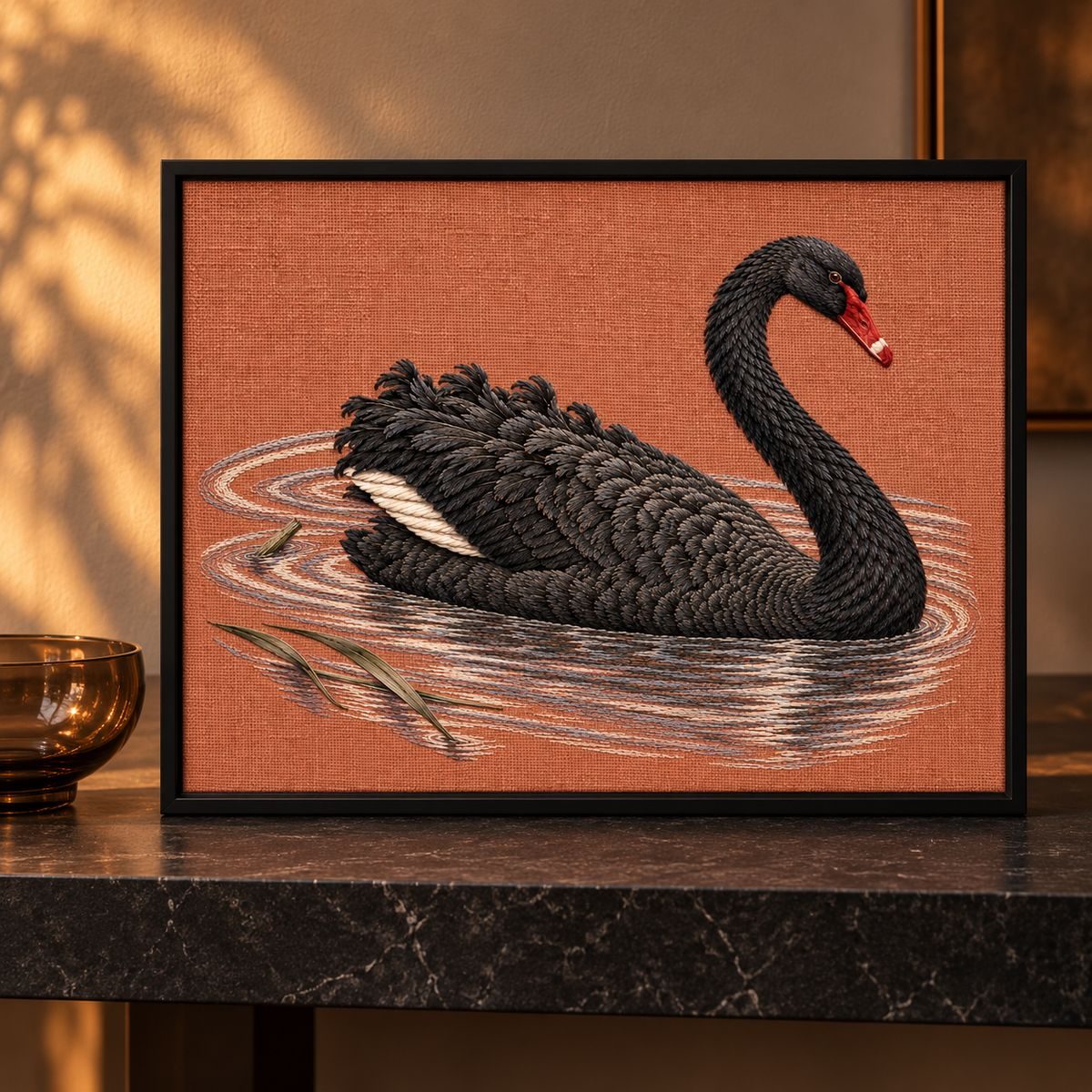 Black Swan embroidery design shown in a digital mockup of A terracotta linen landscape embroidery in a matte black narrow frame, upright on a dark stone console, one low smoked-glass bowl to the side, soft evening light. Study 32.