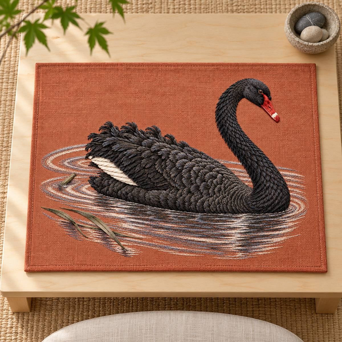 Black Swan embroidery design in a digital mockup of A rectangular terracotta embroidered meditation seat mat lying flat on a low birch platform, near overhead photograph with a small stone bowl outside the mat, full landscape motif. Placement inspiration for Study 32.