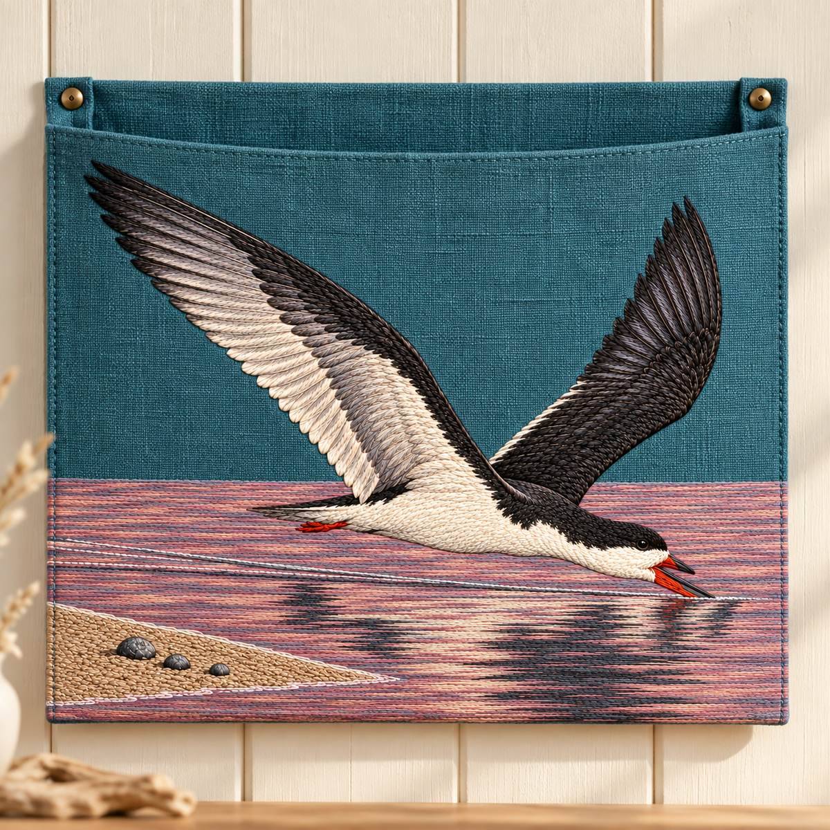 Skimmer embroidery design in a digital mockup of teal linen wide wall organizer with ONE shallow flat pocket whose front carries entire motif, mounted on cream wood, frontal; opening above wing tips. Placement inspiration for Study 37.