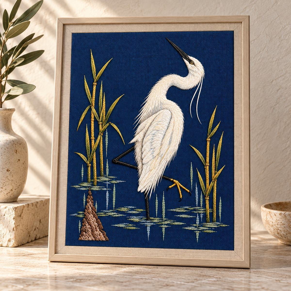 Egret embroidery design in a digital mockup of embroidered blue panel mounted on an archival textile board, leaning upright on a pale stone studio table. Placement inspiration for Study 39.