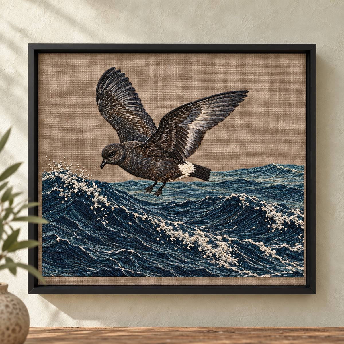 Storm Petrel embroidery design shown in a digital mockup of A landscape embroidery panel in a black metal shadowbox on a pale limewashed wall, narrow visible cloth margins. Study 69.