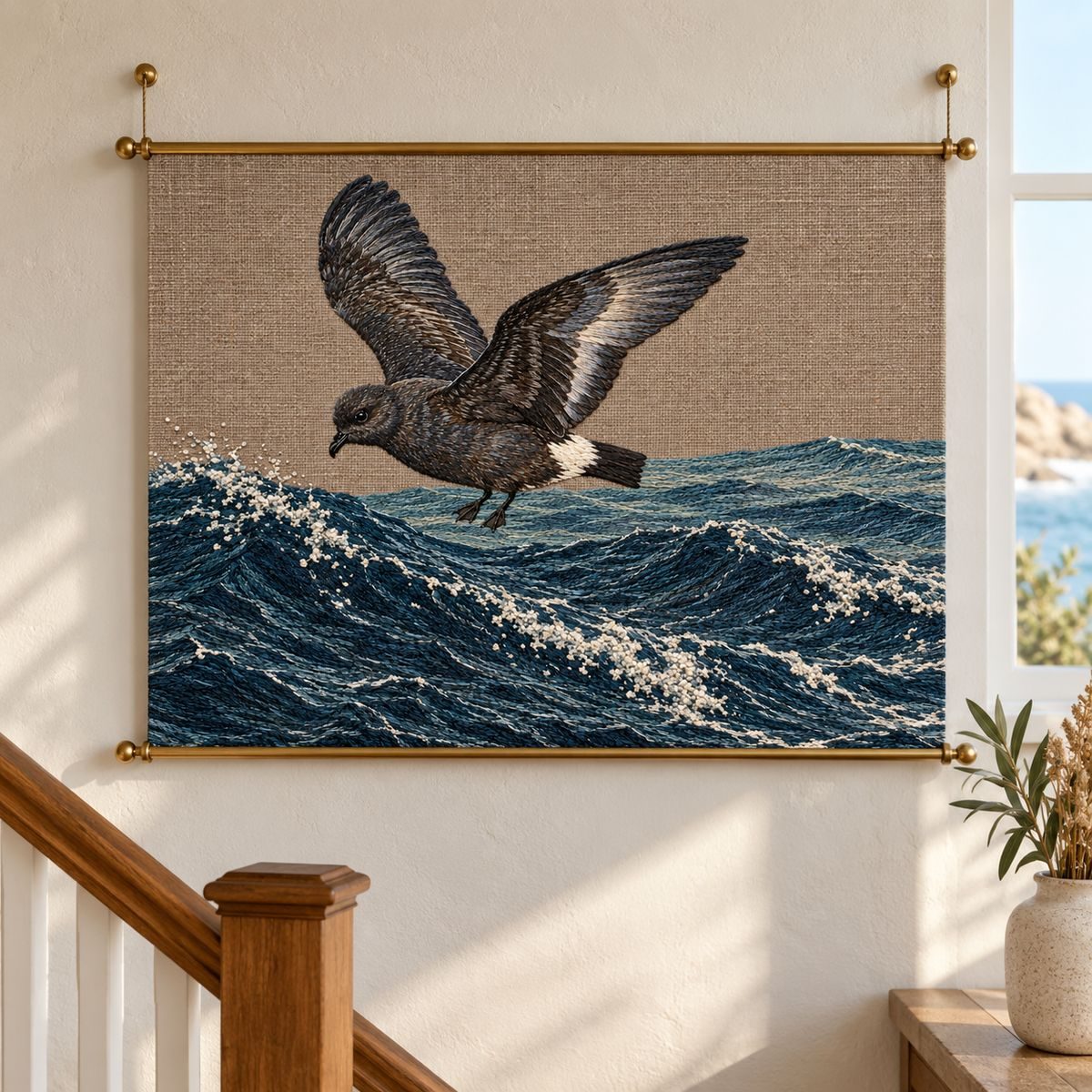 Storm Petrel embroidery design in a digital mockup of A landscape embroidery panel stretched between two thin brass rods in a coastal stair landing, waves remain horizontal. Placement inspiration for Study 69.