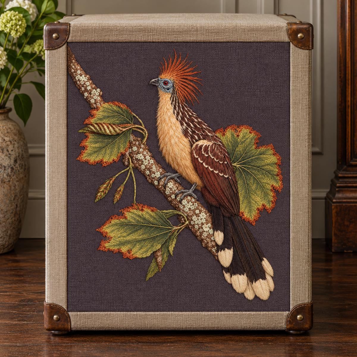 Hoatzin embroidery design in a digital mockup of Aubergine-grey embroidered panel on the broad flat front of a tall rectangular linen storage trunk, dark wood floor, straight-on camera. Placement inspiration for Study 75.