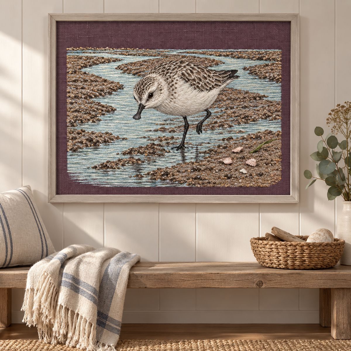 Spoon-billed Sandpiper embroidery design shown in a digital mockup of A landscape aubergine embroidered panel in a pale ash frame above a low coastal hallway bench, complete tide scene shown level and unrotated. Study 77.