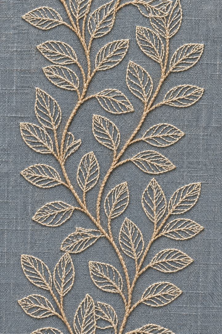 Digital embroidery visualization: warm ivory cotton outlines and fine veins form a repeating leaf border on smoky blue grey linen.
