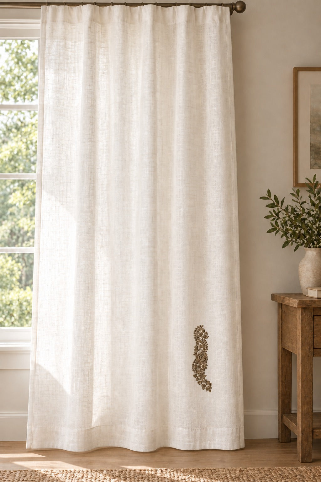 Styled linen curtain panel mockup with a single muted dark bronze brown rose and tulip lace spray embroidered on pale linen; the complete motif has clear fabric around it.