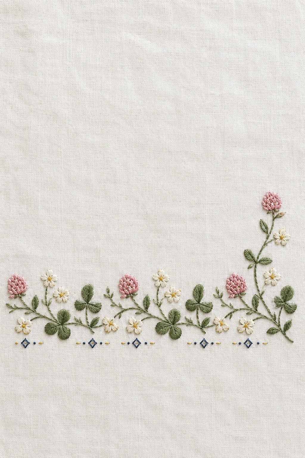 Illustrative embroidery design: Clover and daisies form a low horizontal band on white linen, ending with a taller right-hand stem.