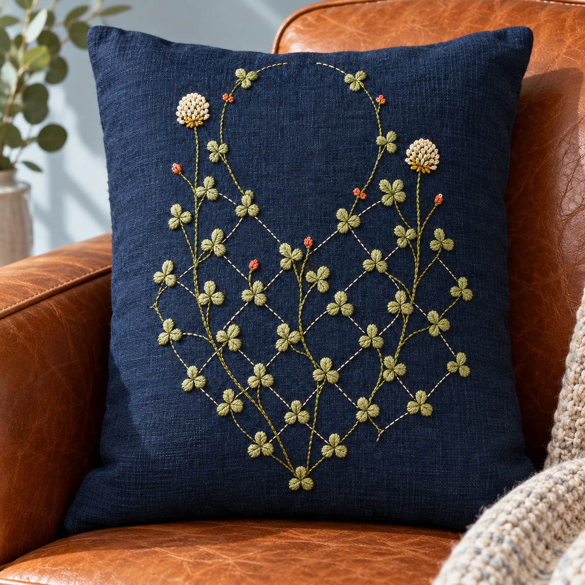 Navy linen cushion mockup featuring the Diamond Clover Lattice hand embroidery design. Clover vines climb through an incomplete diamond lattice on indigo linen.