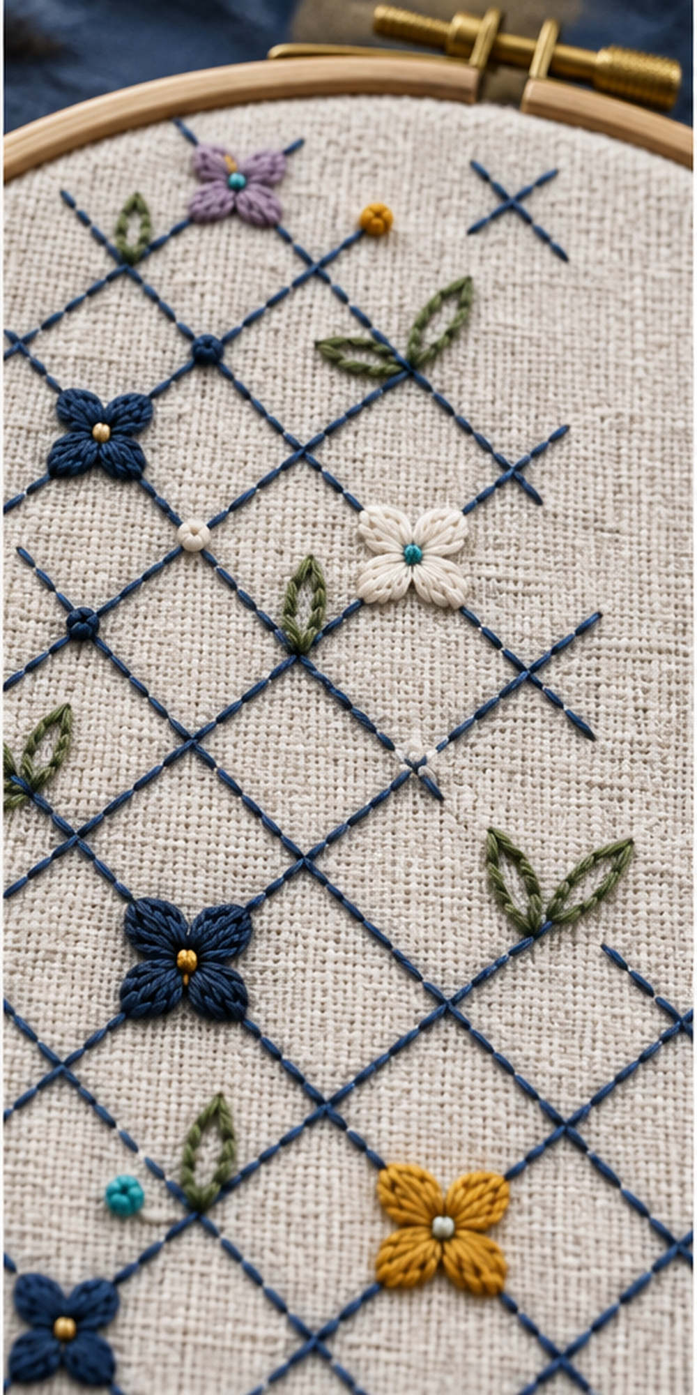 Geometric textile flat lay mockup featuring the Diamond Frost Lattice hand embroidery design. An indigo diagonal lattice carries small rosettes, paired leaves and knot accents beside a clear upper-right square.