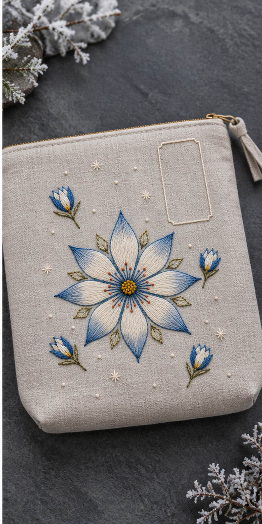 Linen notebook cover mockup featuring the Eight-Petal Snowflower hand embroidery design. A large eight-petal snowflower sits with detached buds and sparse frost stars beside an empty label shape.