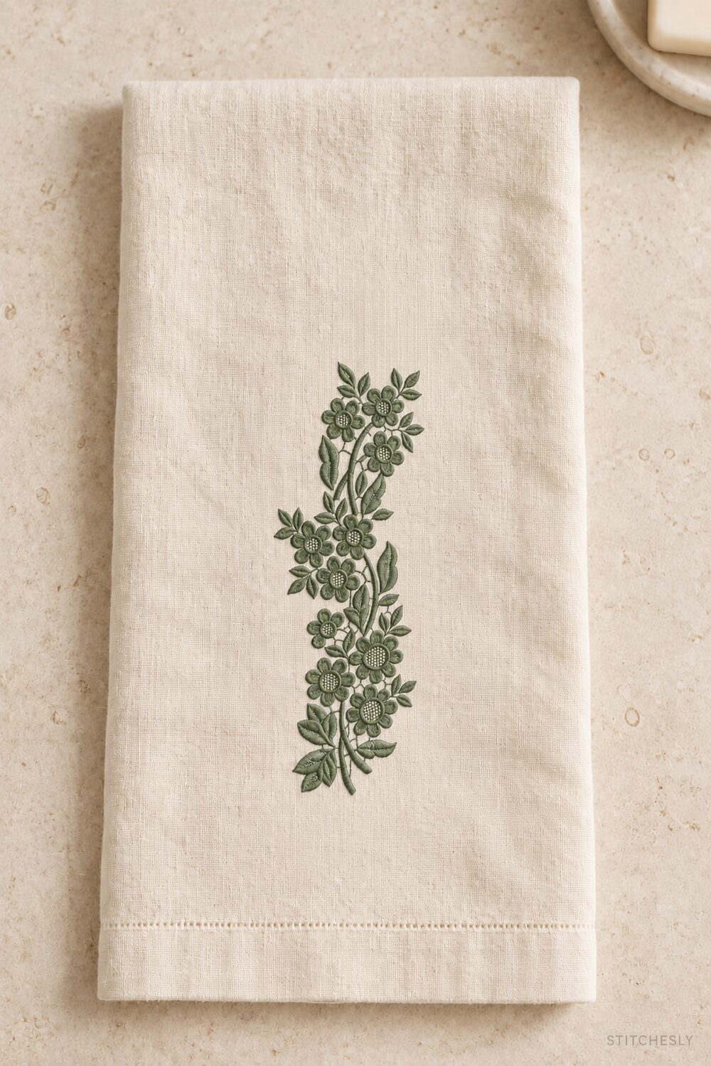 Generated usage mockup of a linen guest towel with the lattice blossom vine machine embroidery motif in one deep muted eucalyptus green thread color.