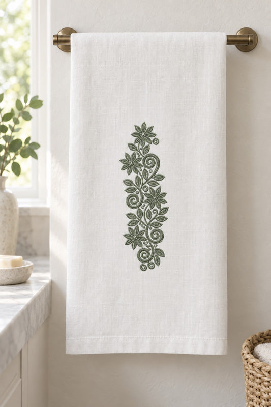 Styled linen hand towel mockup with a single deep muted eucalyptus green starflower scroll vine embroidered on pale linen; the complete motif has clear fabric around it.