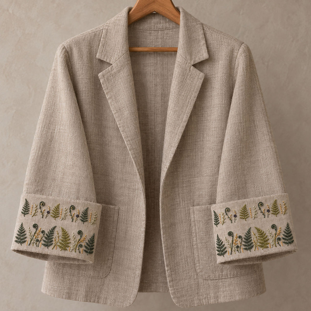 Light linen jacket mockup featuring the Fern Cuff Pair hand embroidery design. Two horizontal bands alternate fern fronds, fiddleheads and fine seed stems.
