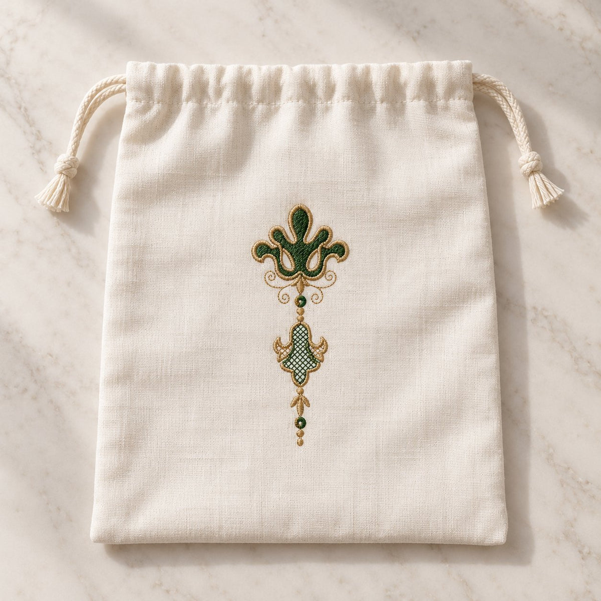 Ivory linen drawstring pouch with a narrow forest-green and champagne fleur de lis pendant embroidered on its front.