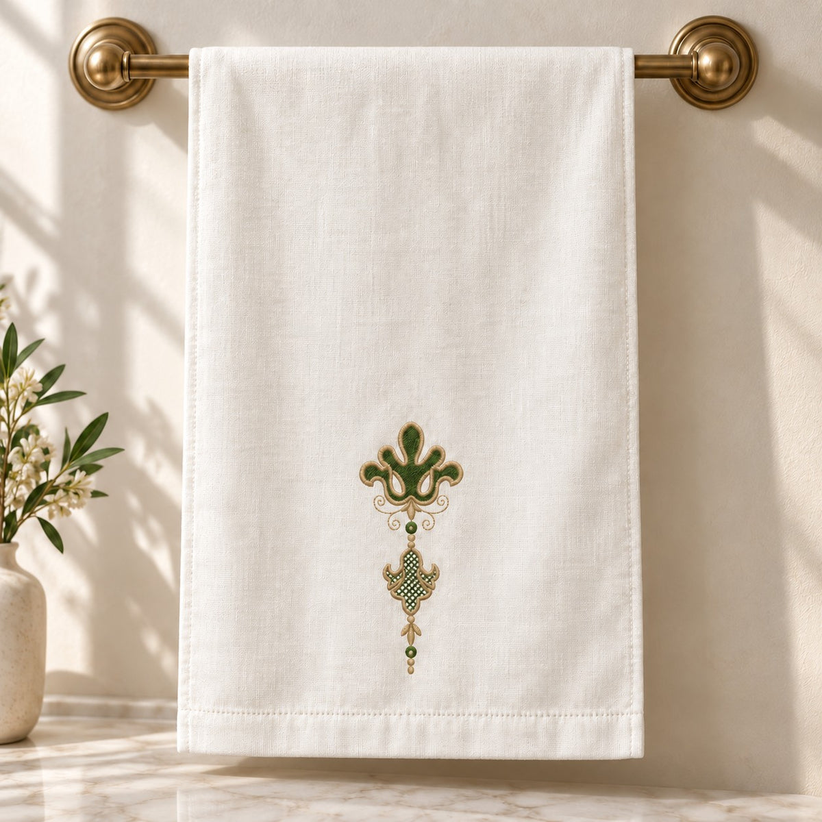 Ivory guest towel hanging from a brass rail with a small green-and-champagne pendant motif above the hem.