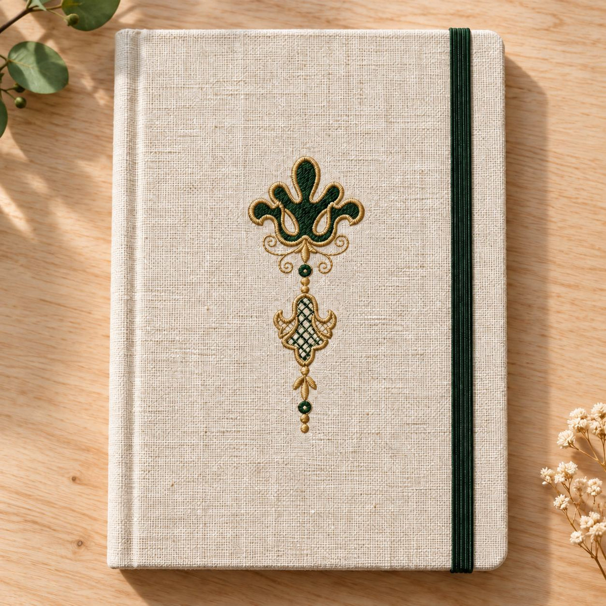 Linen notebook cover with green elastic and a centered forest-green fleur de lis pendant edged in champagne thread.