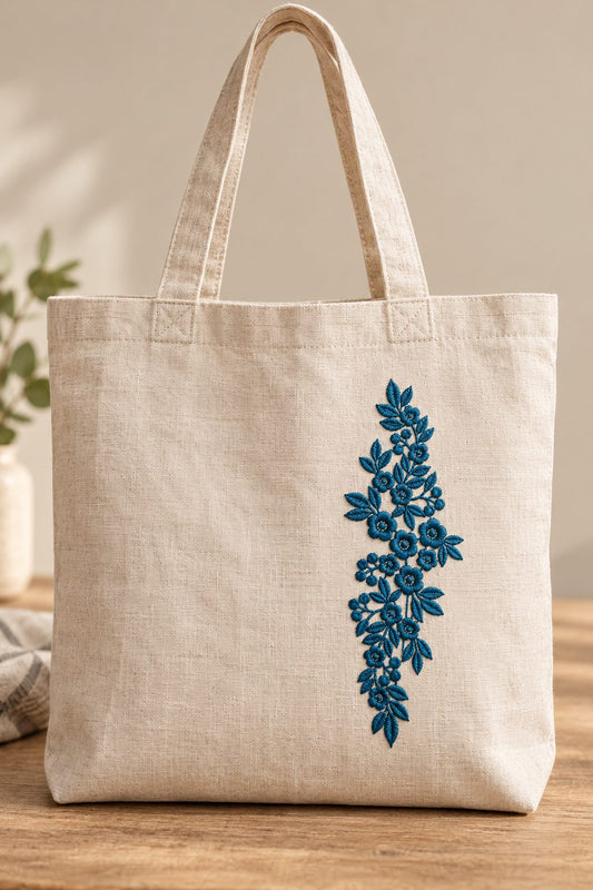 Photorealistic vertical rose leaf spray machine embroidery in deep forest teal thread on a natural linen tote bag, shown as one fabric-stitched motif