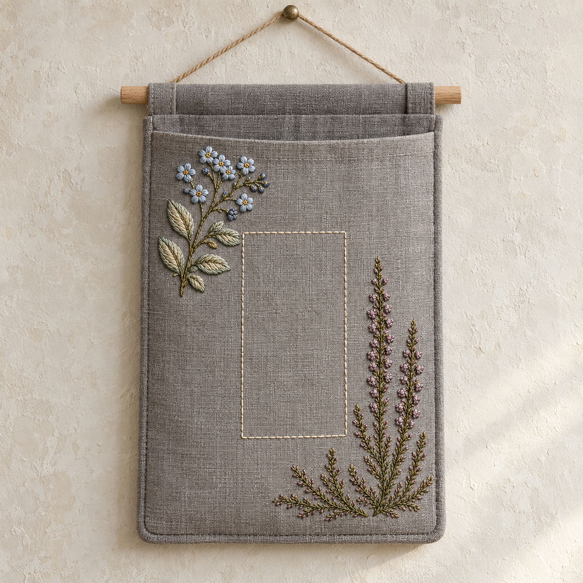 Hanging linen pocket mockup featuring the Forget-Me-Not and Heather hand embroidery design. Blue forget-me-nots cross a mauve heather branch in this small-flower embroidery pattern.