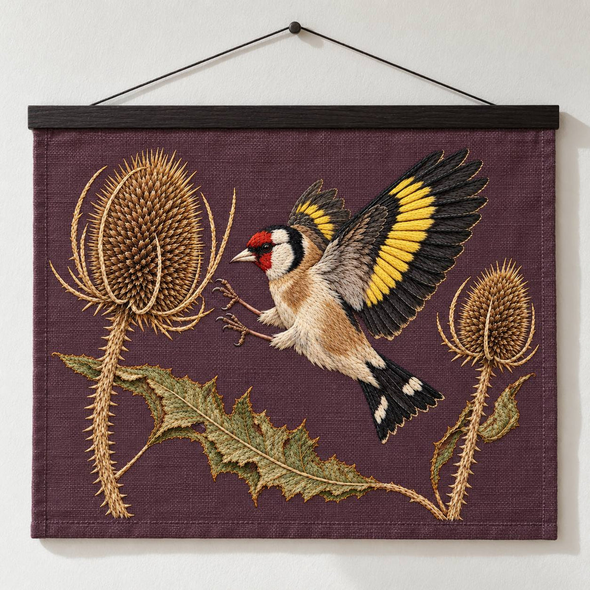 Goldfinch Across the Teasel Crown visual mockup shown as a hanging textile held by wooden rails, with the design on deep muted plum linen.